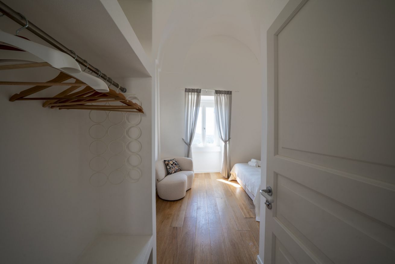Un pasillo con suelo de madera, una cama, una silla y un perchero.