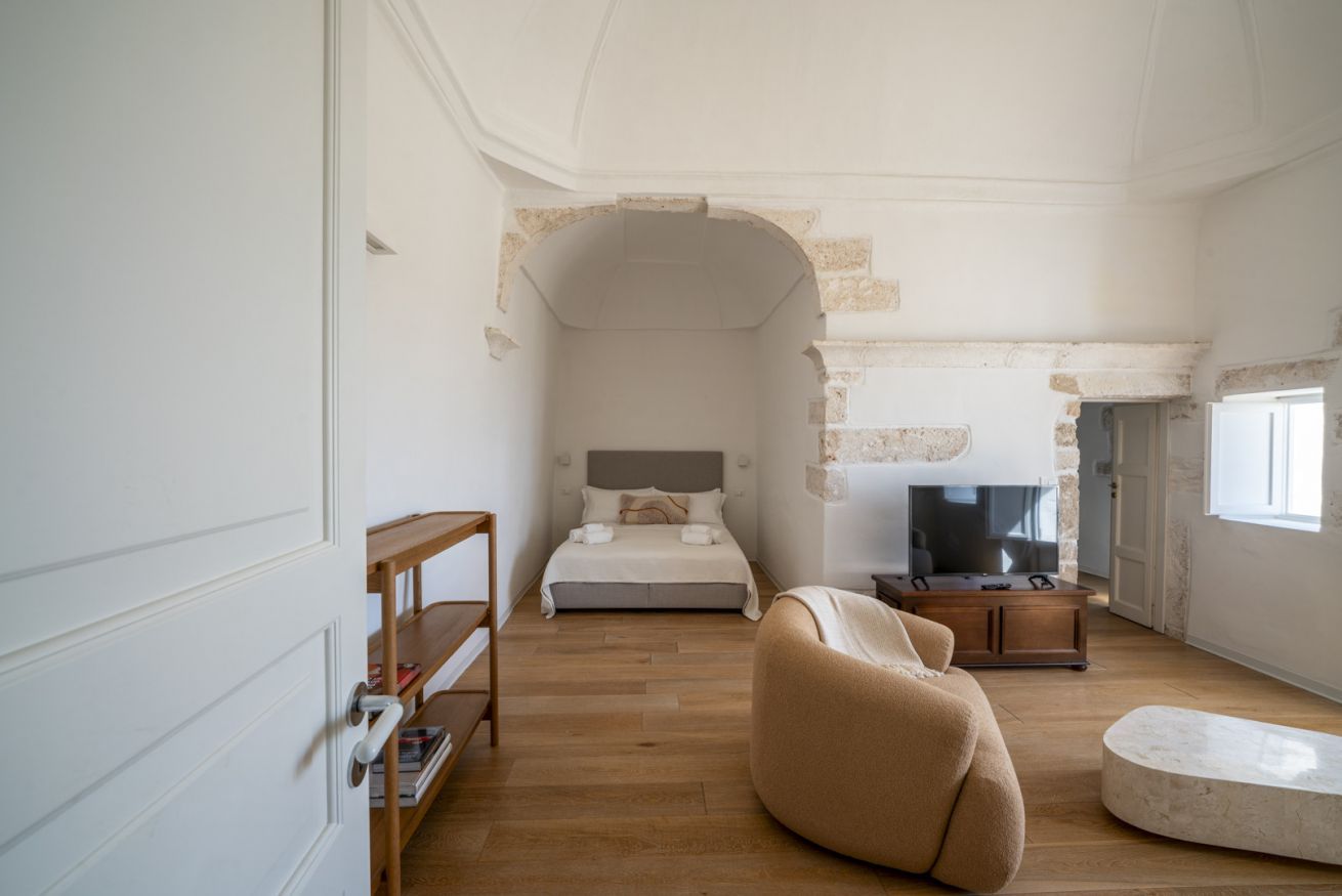 A bedroom with a bed, a TV, a sofa, and a stone archway.