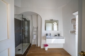 Une salle de bain avec une douche à parois de verre, un meuble-lavabo blanc avec un miroir et un plancher en bois.