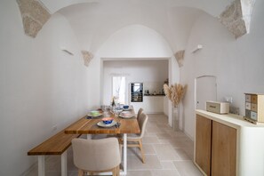 A dining area with a wooden table, chairs, and a kitchen in the background. - Il Palazzotto: Historic Residence with Sea View in Ostuni (Ostuni)