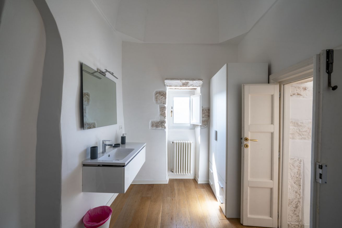 Un couloir étroit avec une porte blanche, un radiateur blanc et une fenêtre dotée d’un cadre en pierre.