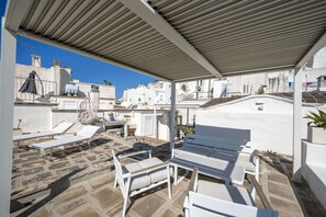 A rooftop terrace with white lounge chairs, a table, and a hanging chair.
