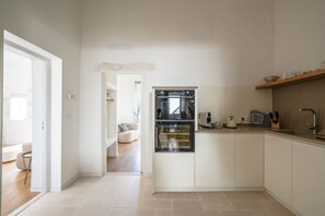 Une cuisine moderne avec des meubles blancs, un four encastré et un plan de travail sur lequel se trouvent une bouilloire et des ustensiles.