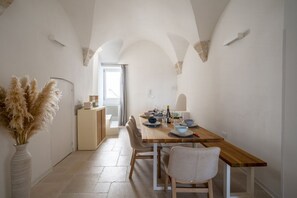Un coin repas avec une table en bois dressée pour quatre personnes, un vase rempli de plumes d’herbe des pampas et une vue sur un balcon.