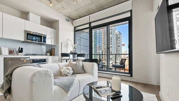 A modern living room with a sofa, a glass coffee table, and a view of tall buildings.