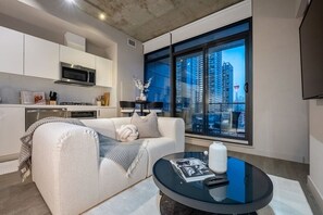 Uma sala de estar moderna com sofá, mesa de centro, área de cozinha e uma janela grande com vista para a cidade.
