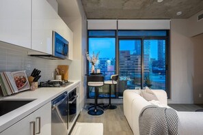 Uma cozinha moderna com área de jantar, sofá e uma grande janela com vista para a cidade.