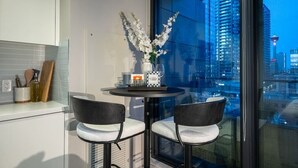 A modern kitchen with a dining area, a vase with flowers, and a city view through large windows.
