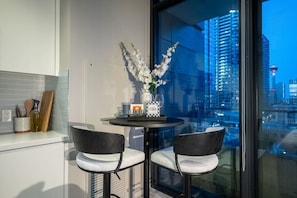 Uma cozinha moderna com área de jantar, um vaso com flores e vista para a cidade através de amplas janelas.