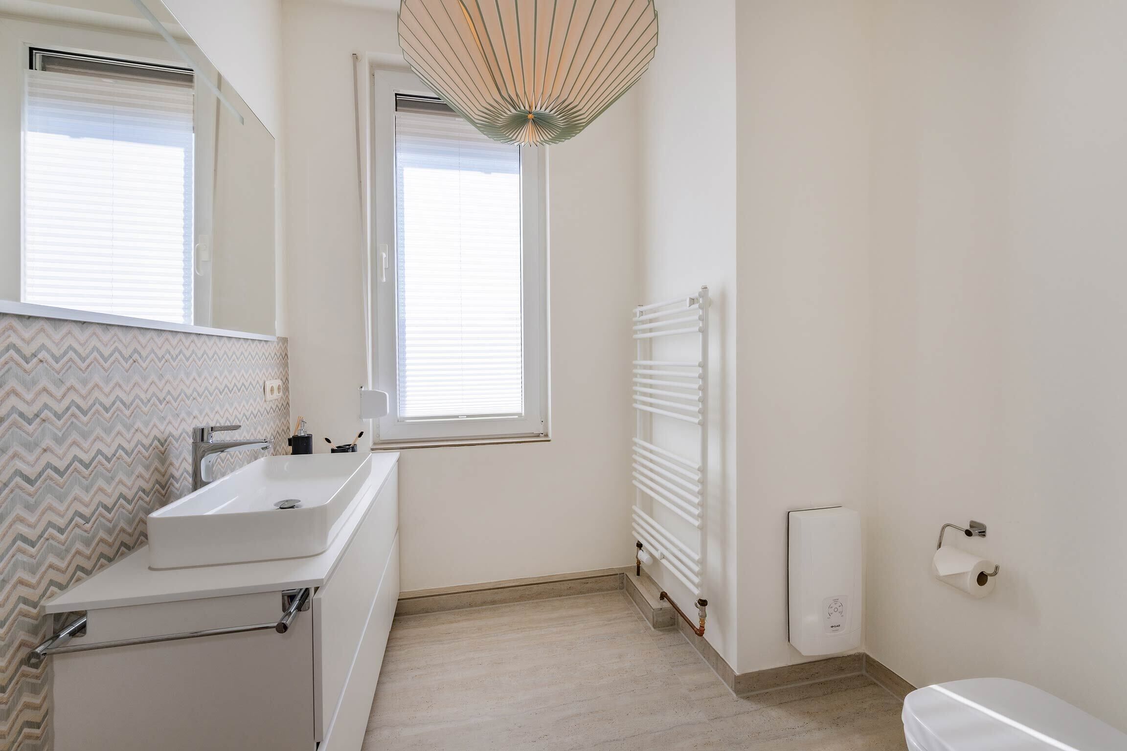 Un baño moderno con lavamanos, espejo y retrete blancos.