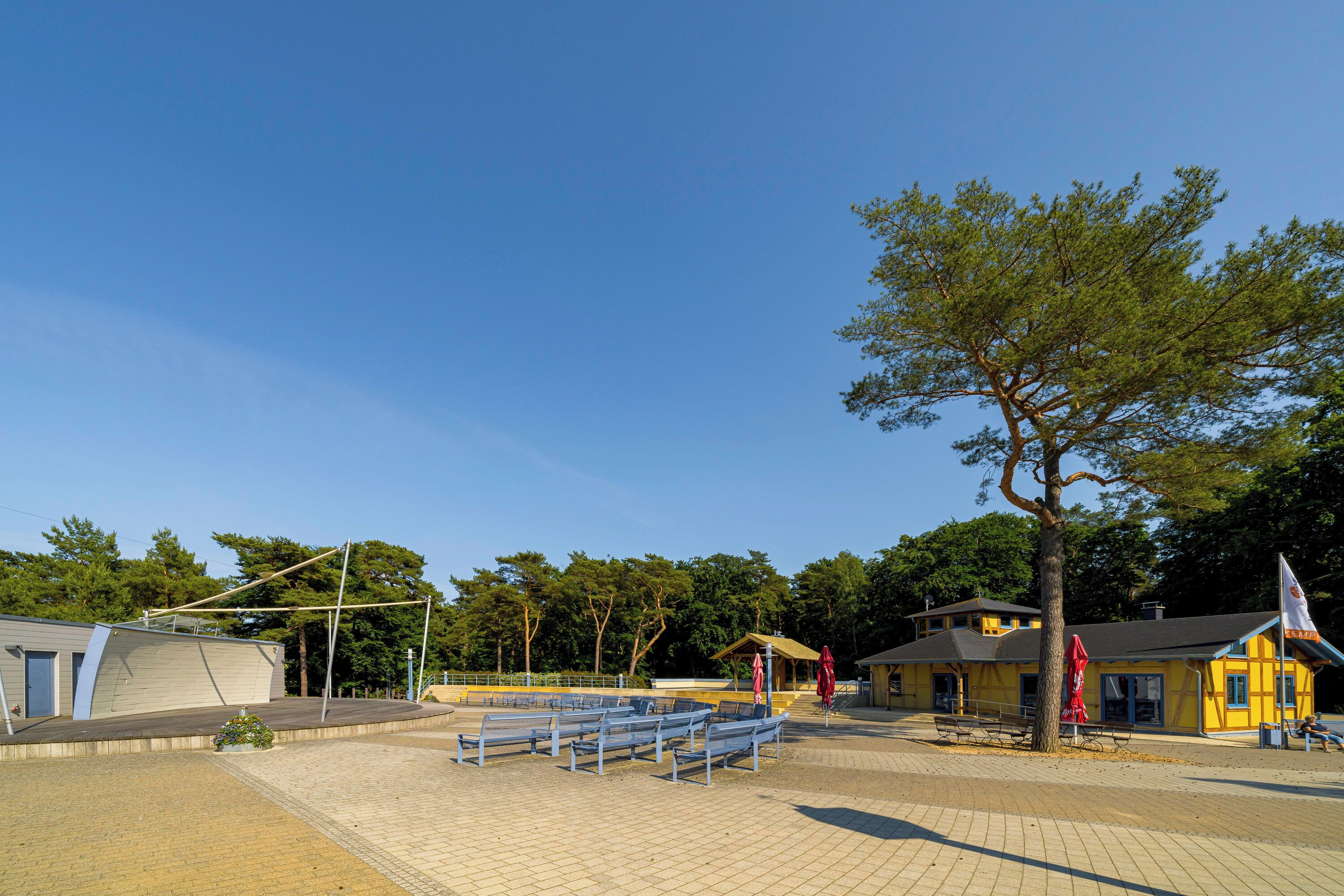A paved area with benches, a flagpole, and a yellow building with a flag.