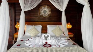 A bed with a canopy, two nightstands, a decorative wall piece, and a heart-shaped towel arrangement. - Eco Oasis Wooden Villa (Tegallalang)
