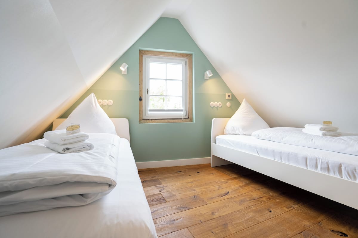 Une chambre avec deux lits, une fenêtre et un plancher en bois.