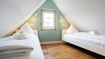 A room with two beds, a window, and wooden flooring.