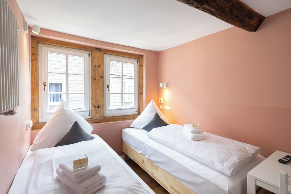 Une chambre avec deux lits, une tête de lit en bois, une table de chevet et une fenêtre avec des volets.