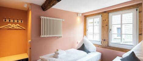 A bedroom with two beds, a radiator, a window with wooden shutters, and a wall-mounted light fixture.
