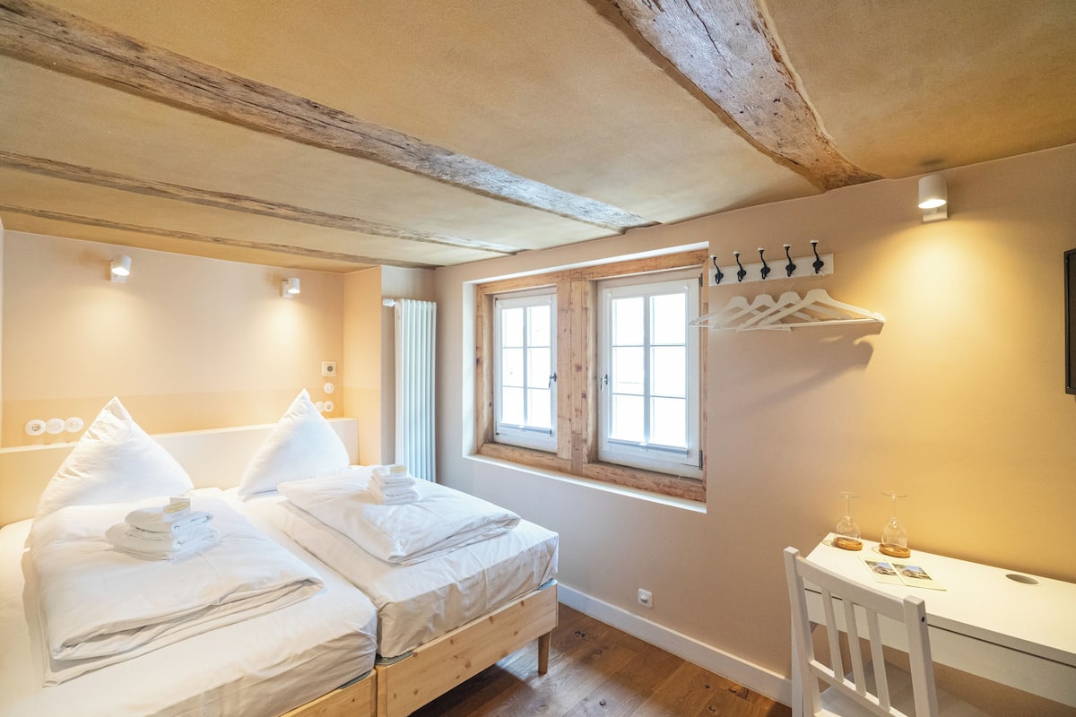 Une chambre avec deux lits, un bureau en bois et une fenêtre avec des volets en bois.
