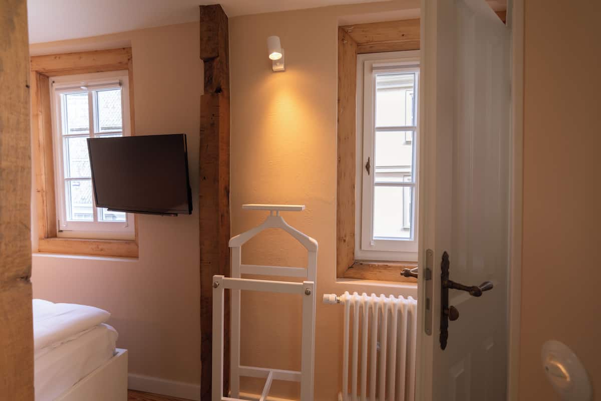 Une chambre avec un lit, un téléviseur fixé au mur, un radiateur et une porte dotée d’une poignée.