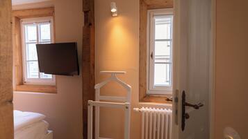 Una habitación con cama, televisor montado, radiador y una puerta con manija.