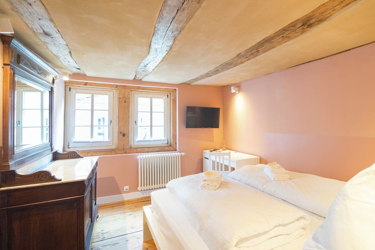 Une chambre avec un plafond en bois, un lit avec du linge de lit blanc, une commode, un téléviseur fixé au mur et une fenêtre donnant sur un beau paysage.
