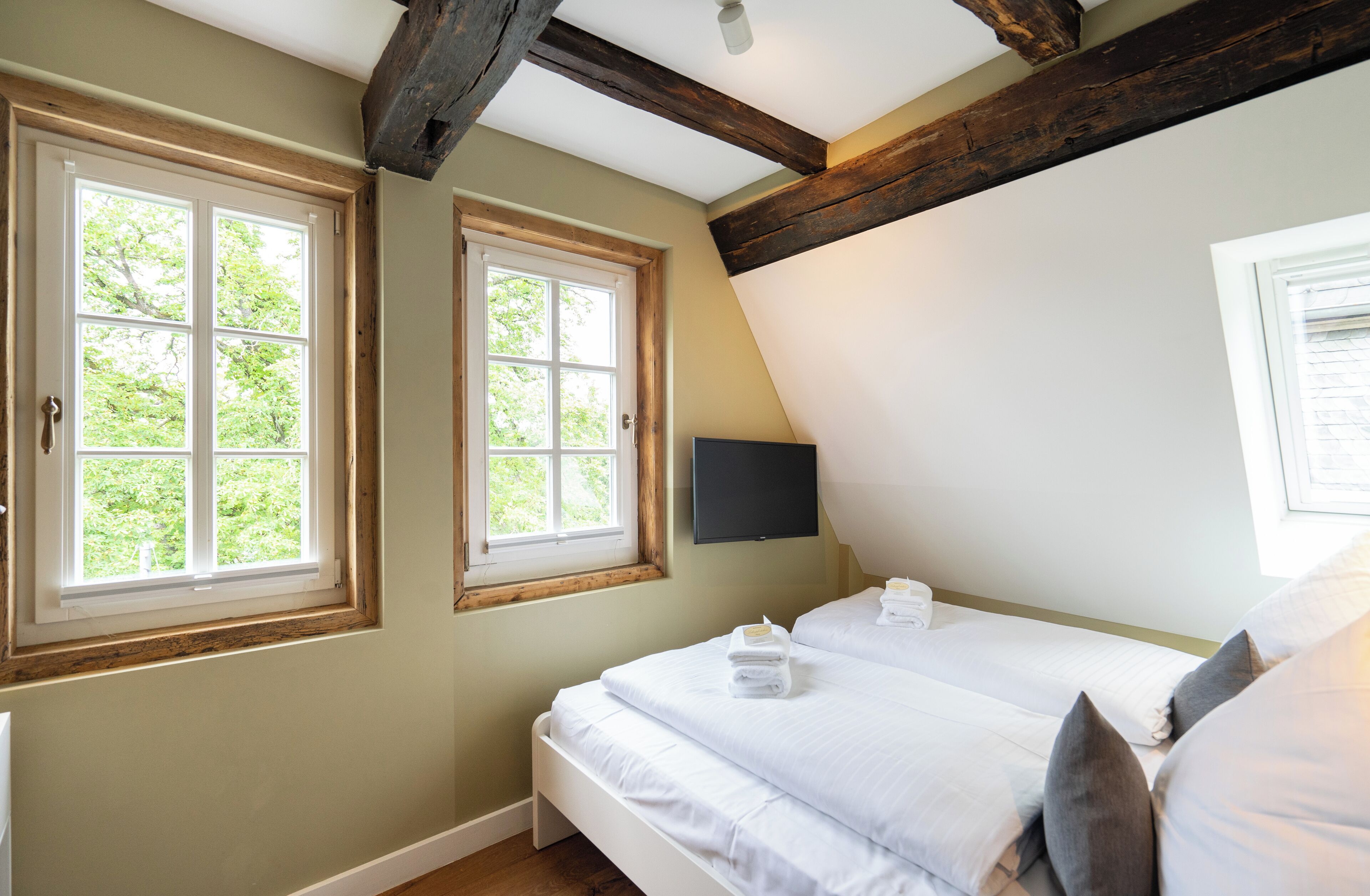 Dormitorio con dos camas, ventanas amplias, televisor de pantalla plana y vigas de madera a la vista.