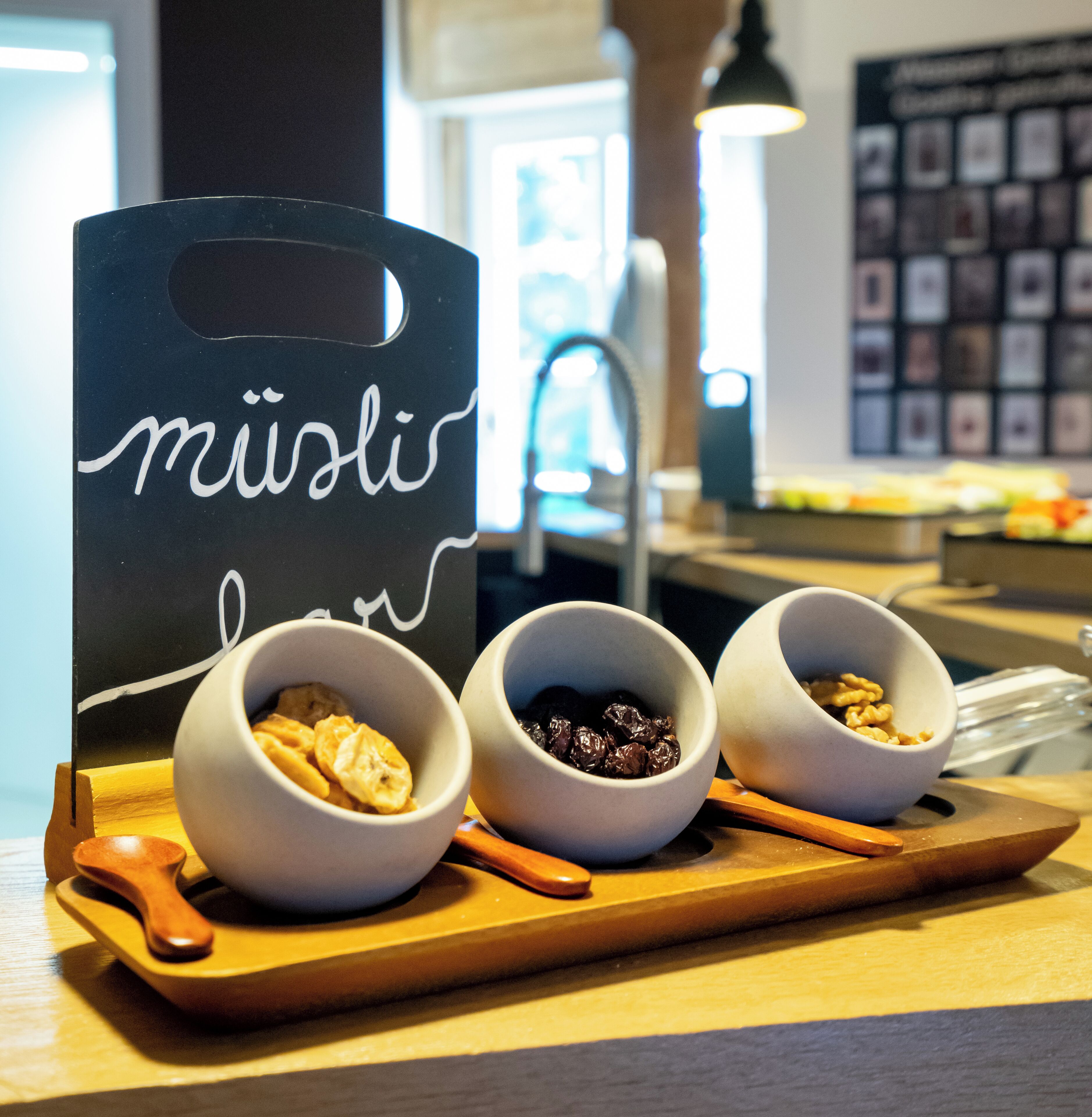 A tray with three bowls containing different food items, a sign with the word "müsli", and a wooden spoon.