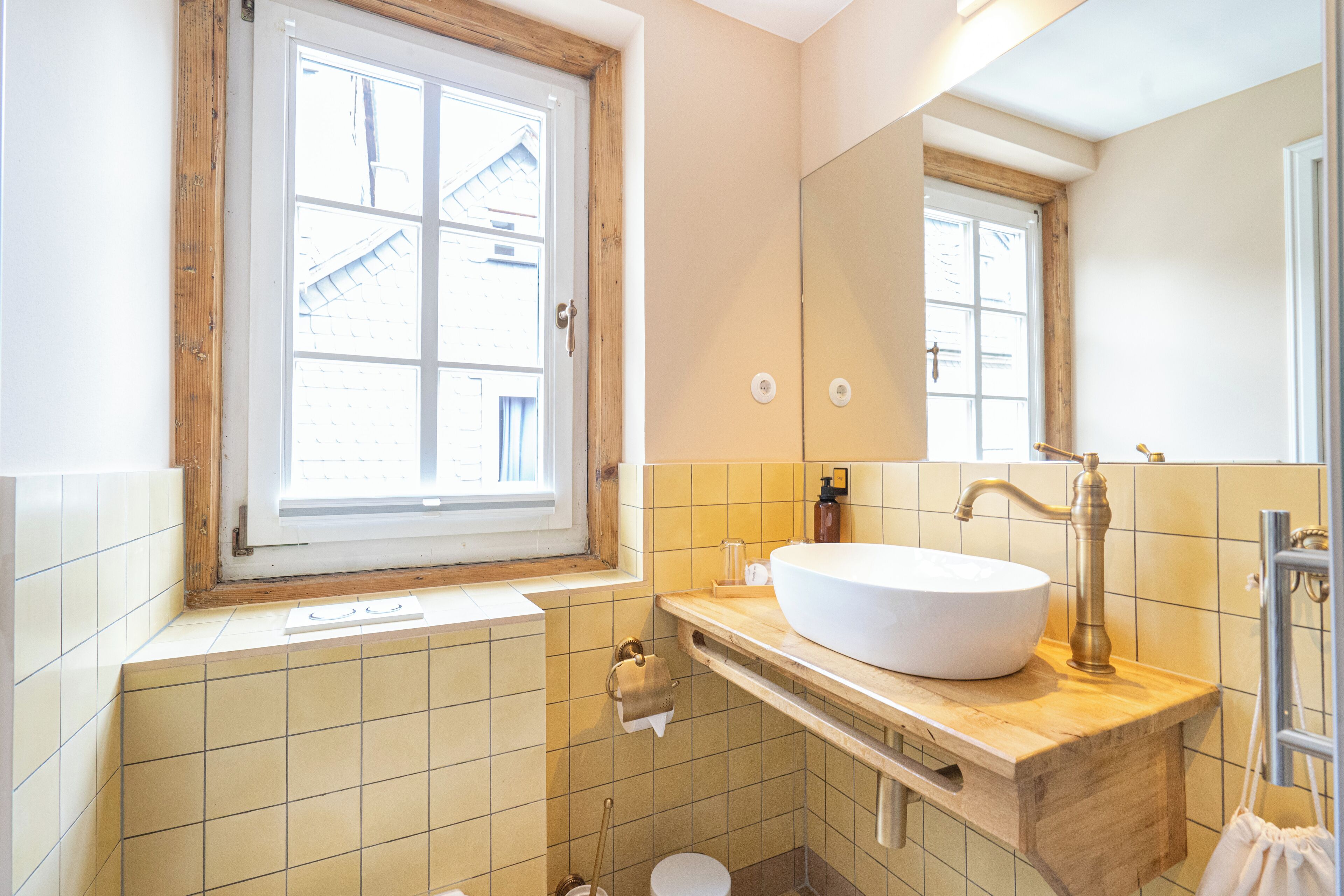 A bathroom with a large window, a white sink, and a mirror.