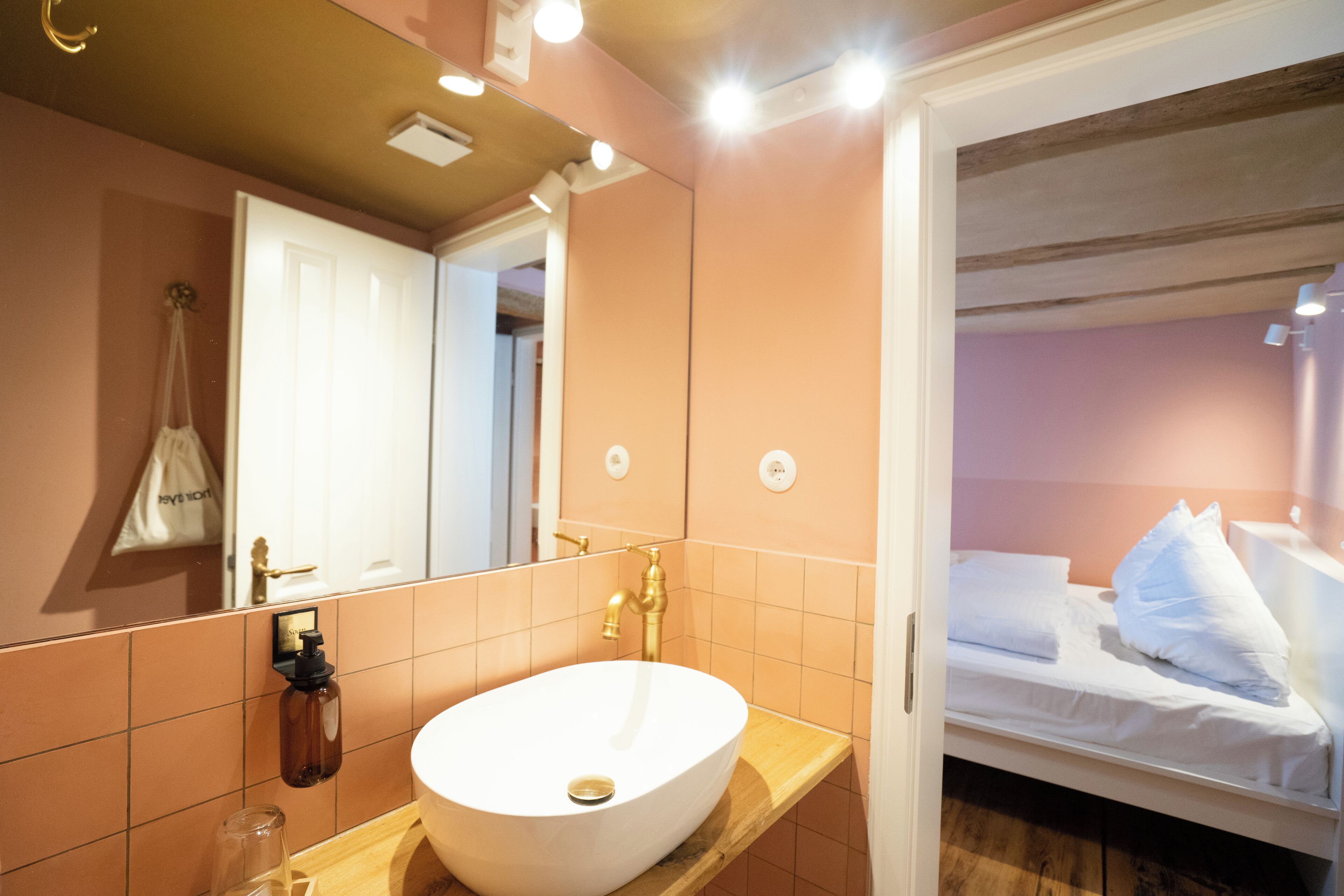 A bathroom with a white sink, a mirror, and a wooden shelf.