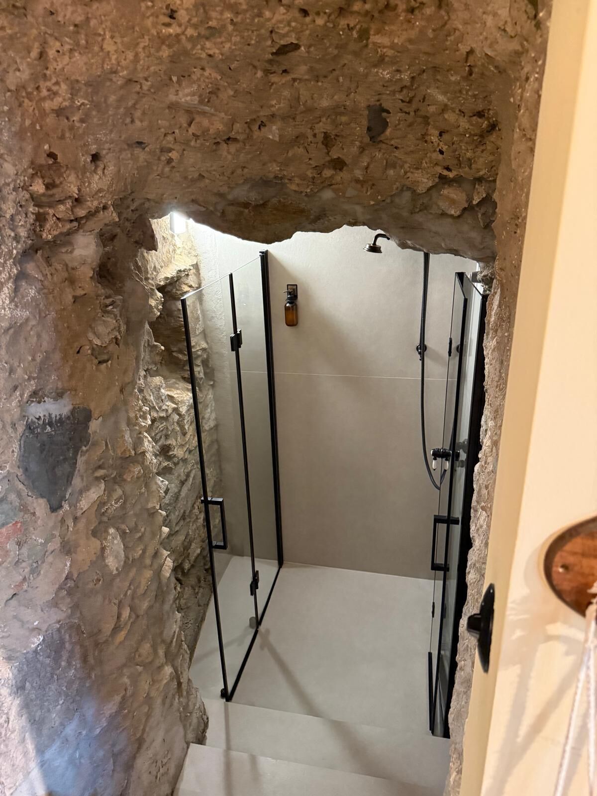 Eine Dusche mit Steinwänden, einer Glastür und einem weißen Fliesenboden.