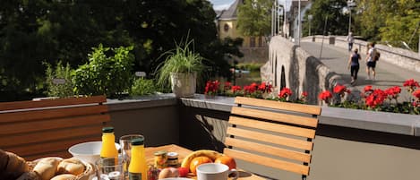 A wooden table with breakfast items, a bench, and a view of a bridge and church.
