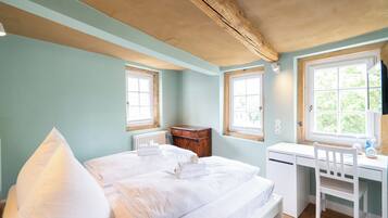 A bedroom with a bed, a desk, and two windows.