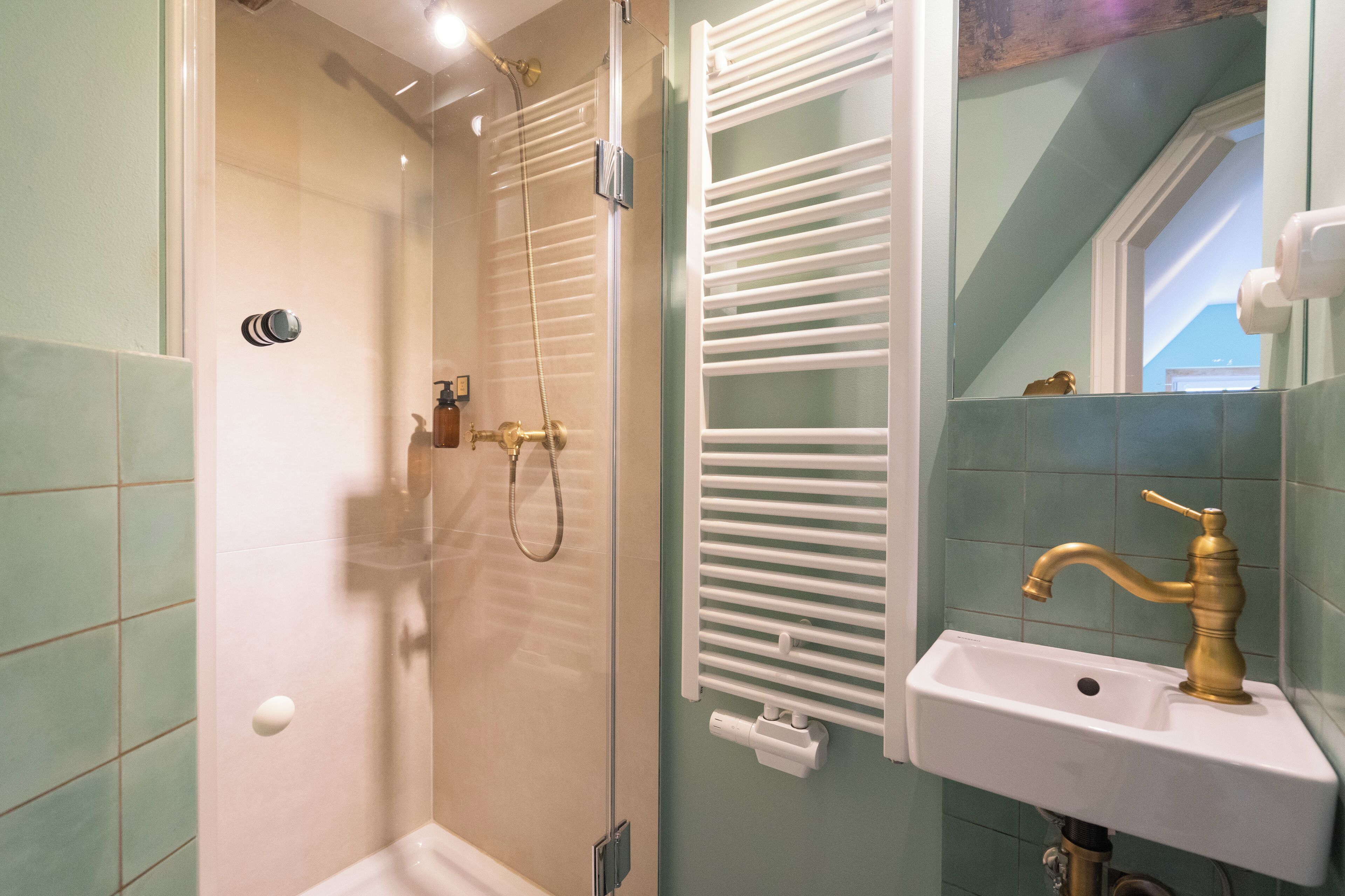 Une salle de bain dotée d’une douche à parois de verre, d’un lavabo blanc avec un robinet doré et d’un porte-serviettes avec des serviettes blanches.