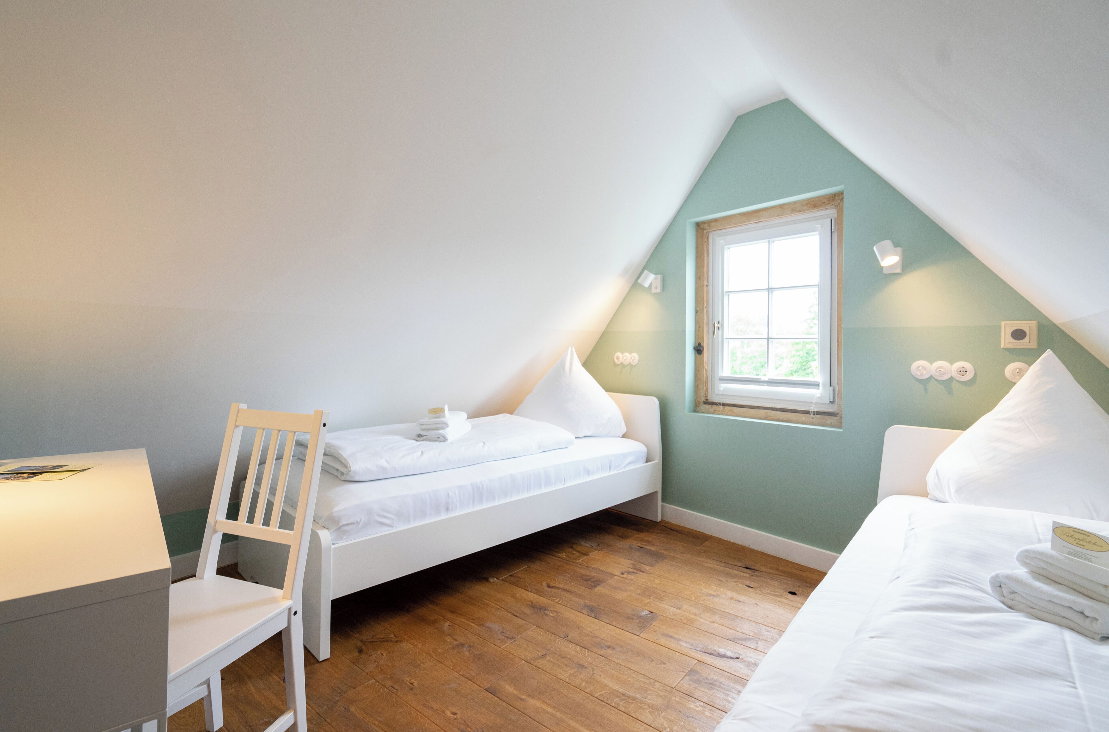 A small, cozy room with a sloped ceiling, a single bed, a chair, and a desk.
