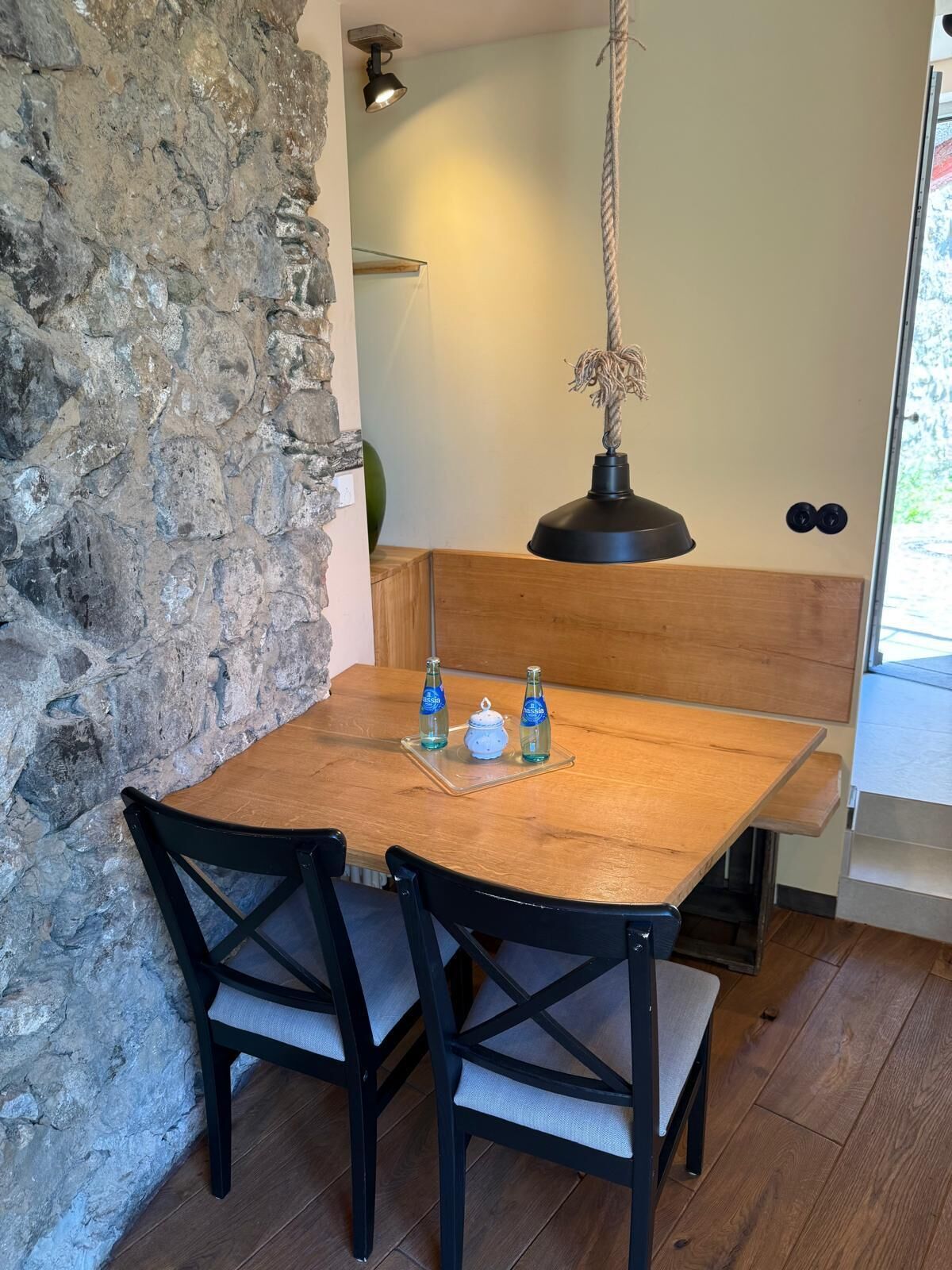 Una mesa de comedor de madera con dos sillas, una lámpara colgante y una pared de piedra.