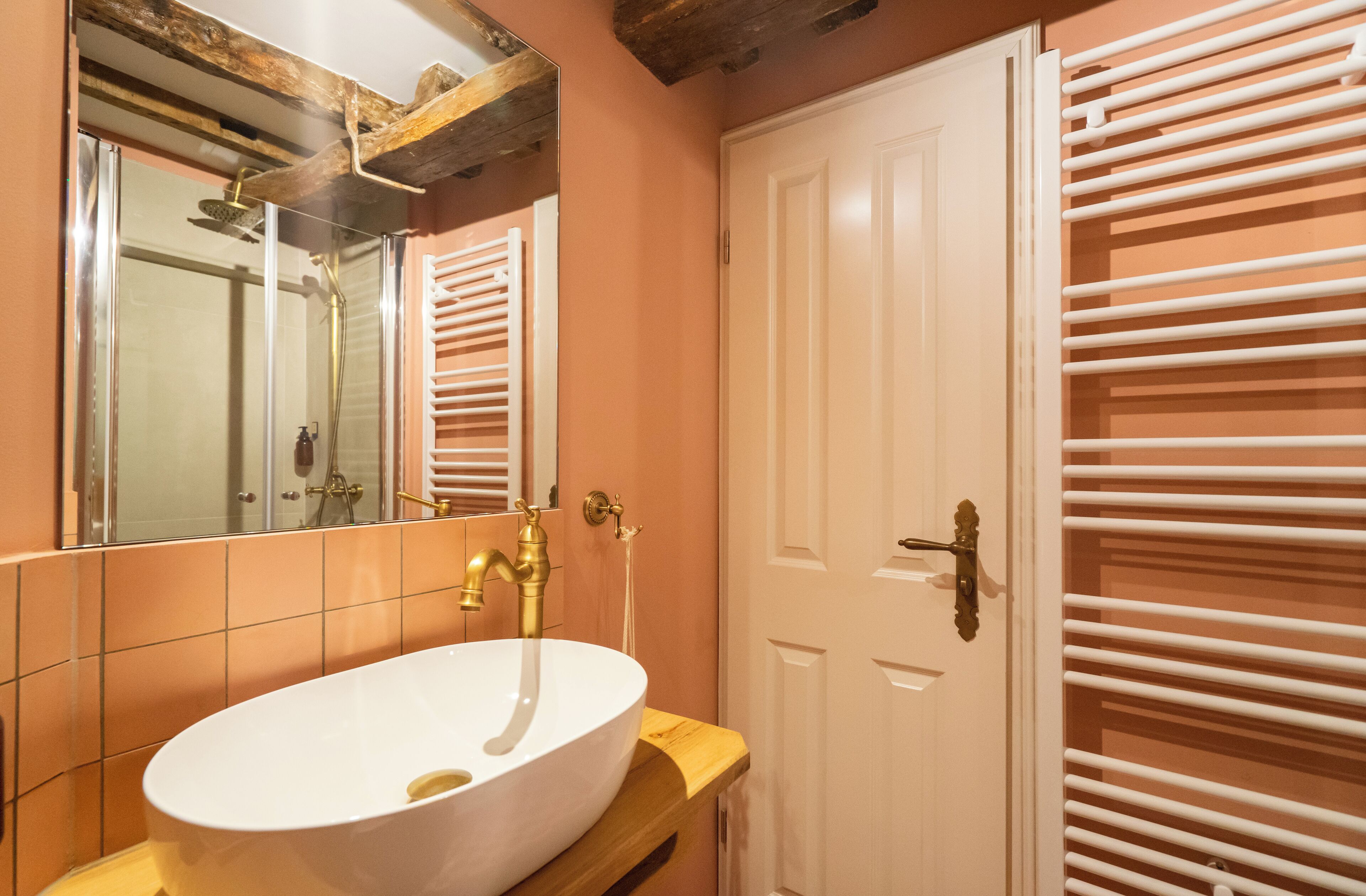 Une salle de bain avec un lavabo blanc, un miroir et une porte dotée de porte-serviettes.
