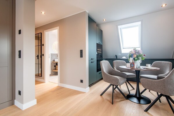 A modern kitchen with dark cabinets, a dining area with a round table and four chairs, and a large window providing natural light.