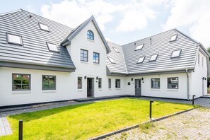 Une maison moderne à deux étages, dotée d’une architecture symétrique, avec une entrée centrale, un petit porche et une pelouse bien entretenue.