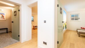 A hotel corridor with a bench, a poster, and a door leading to a room with a window and a bed. - F'27 Living, Whg. 06 - F27 Living (Sylt)