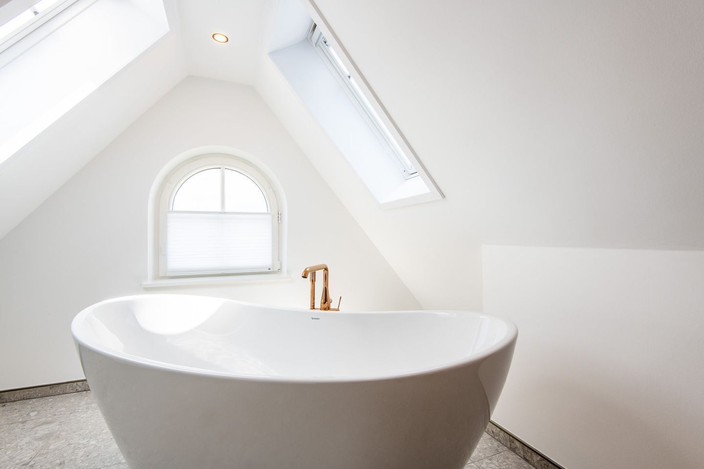 A modern bathroom with a freestanding bathtub, skylight, and a window.