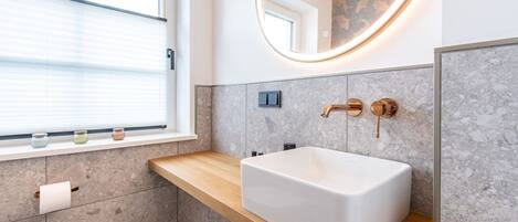 Un baño moderno con un lavamanos grande y rectangular, una encimera de madera, una ventana con persianas y un espejo instalado en la pared.