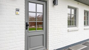 Een wit bakstenen gebouw met een grijze deur, voorzien van een raam en een codeerapparaat.