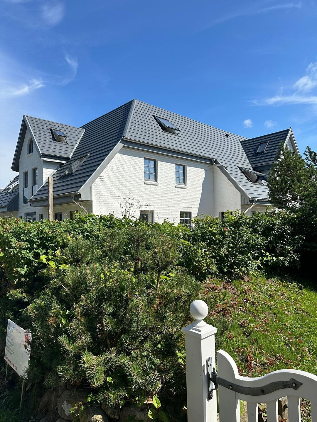Ein großes, weißes, zweistöckiges Haus mit einem steilen Dach und mehreren Oberlichtern.