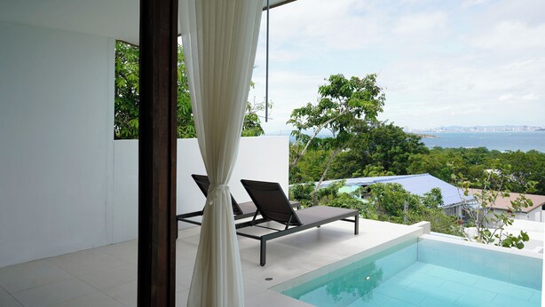 A modern outdoor pool area with two lounge chairs, a clear view of the sea, and lush greenery in the background. - Pichcha Kohlarn (Koh Lan)