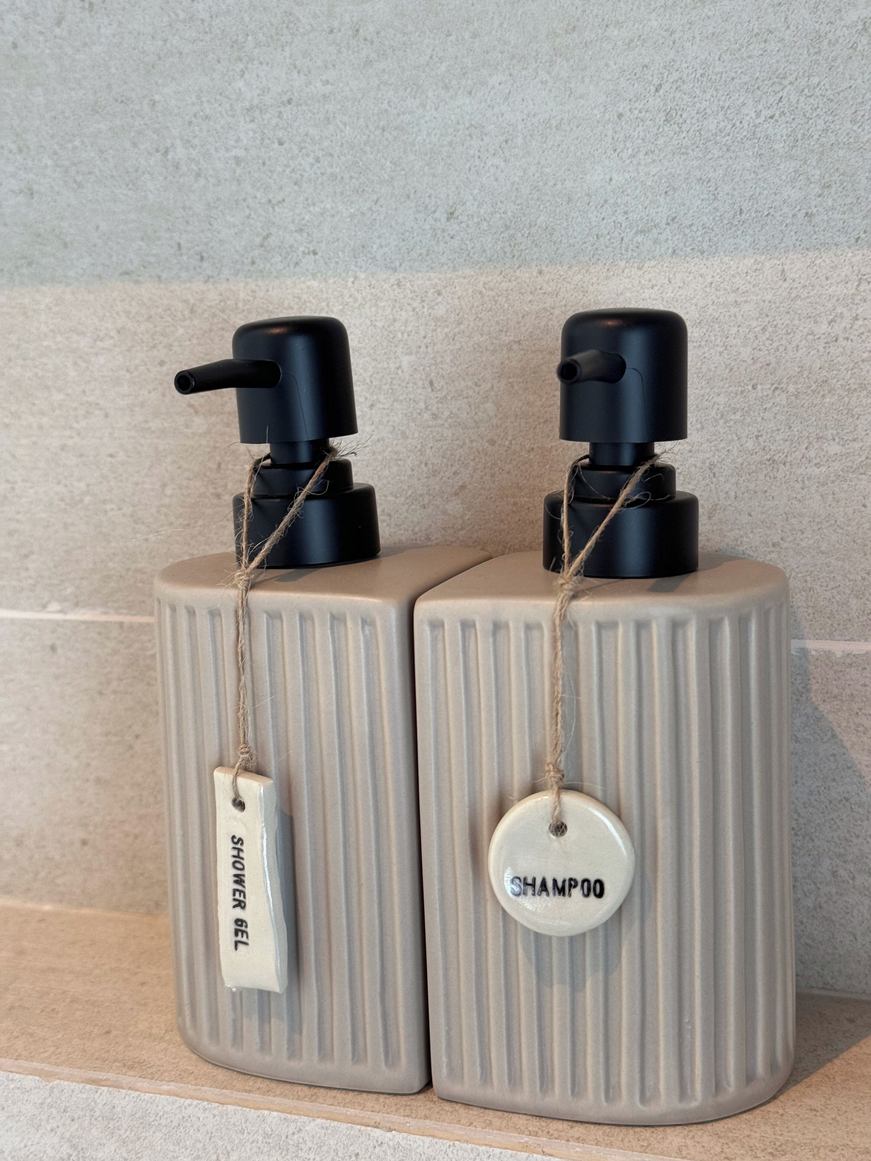 Two toiletry bottles with pumps, one labeled 'SHOWER GEL' and the other 'SHAMPOO', placed on a textured surface.