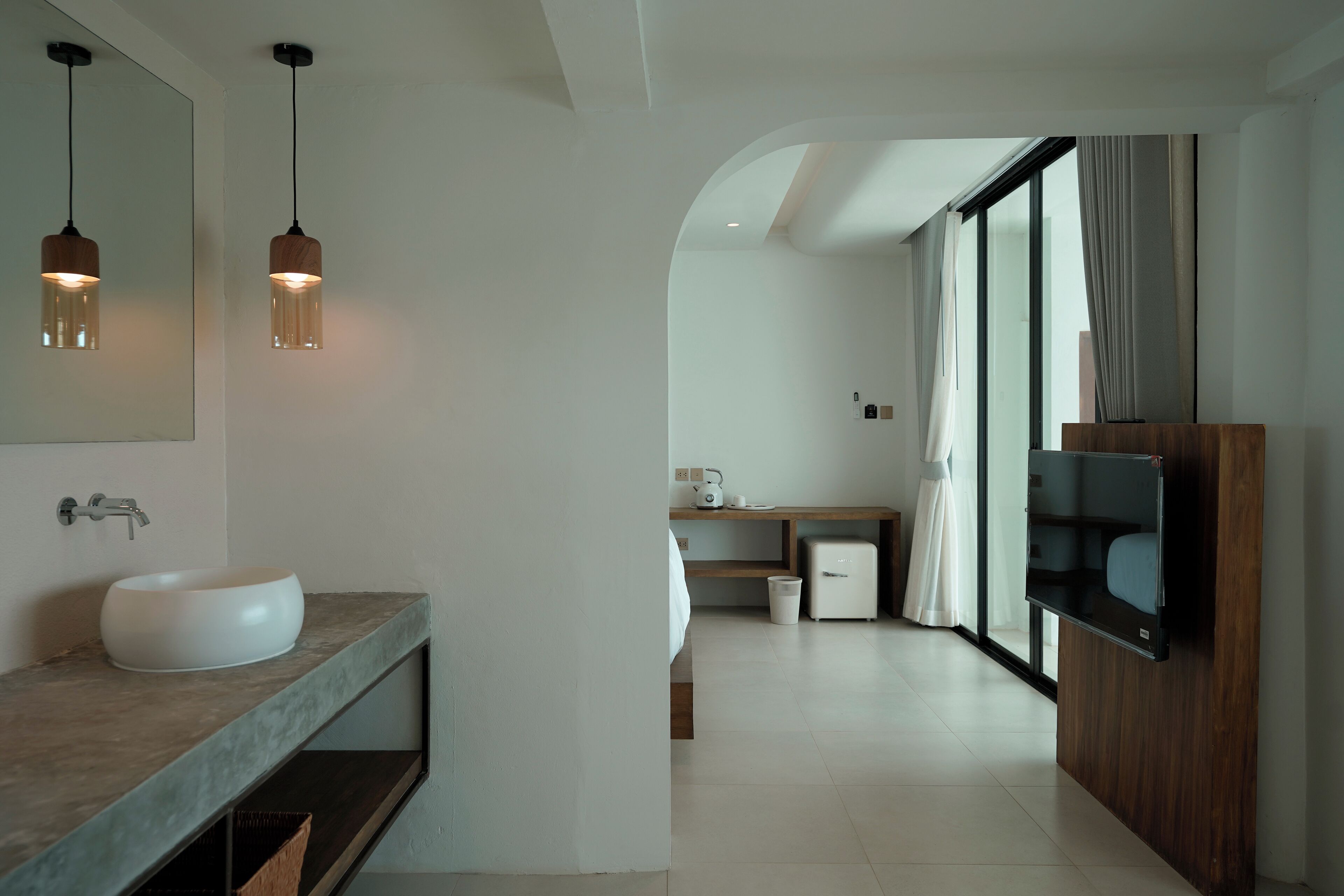 A modern bathroom with a large mirror, two pendant lights, a white sink, and a wooden vanity.