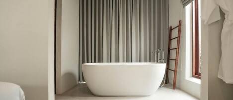 A modern bathroom with a freestanding bathtub, a wooden ladder, and a window with curtains.