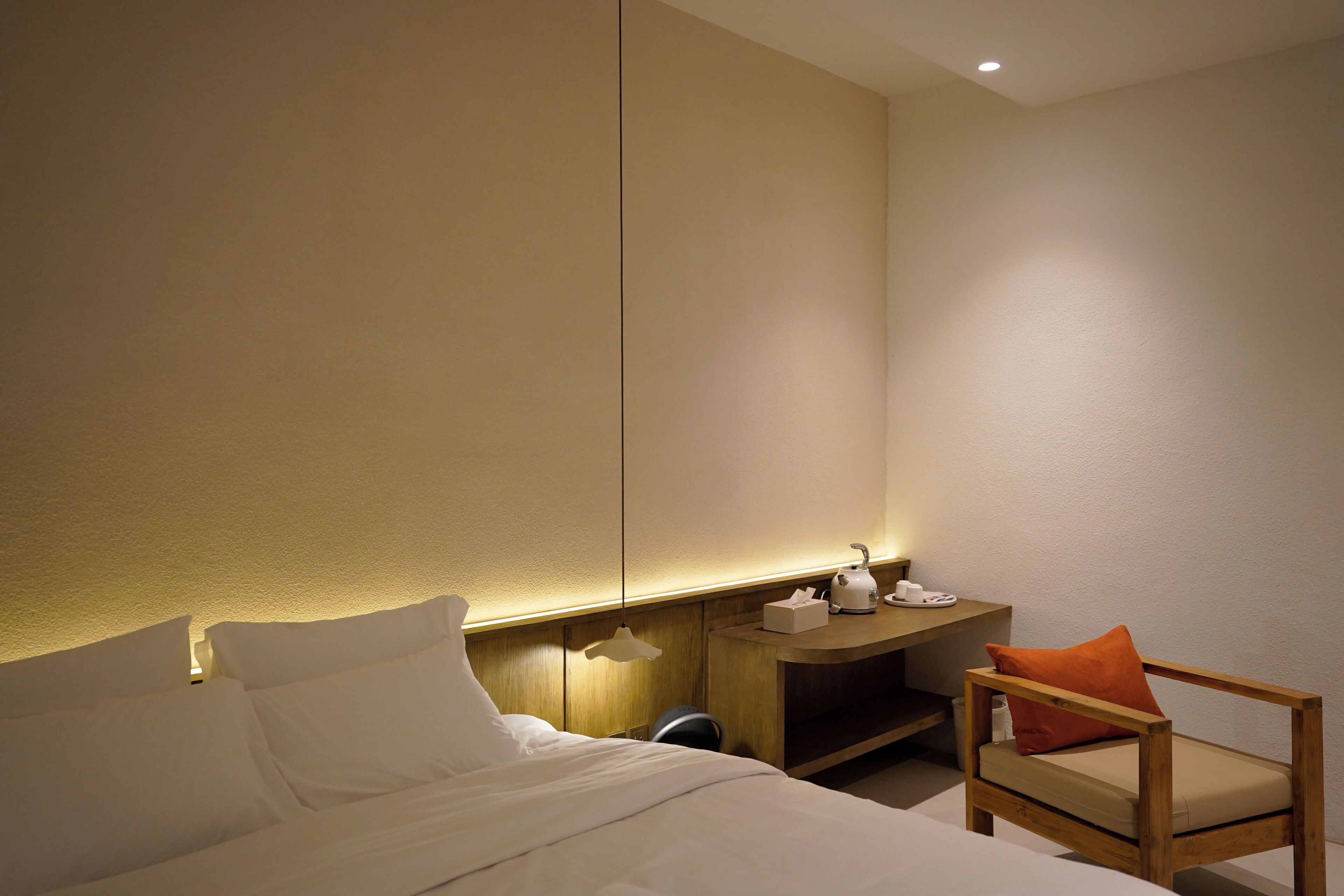 A hotel room with a bed, a wooden nightstand, a chair, and a wall-mounted shelf.