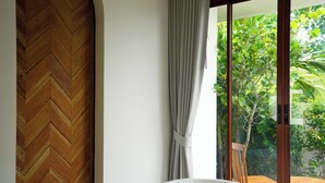 A modern bathroom with a herringbone wood floor, a white bathtub, and a view of lush greenery through a sliding glass door. - Pichcha Kohlarn (Koh Lan)