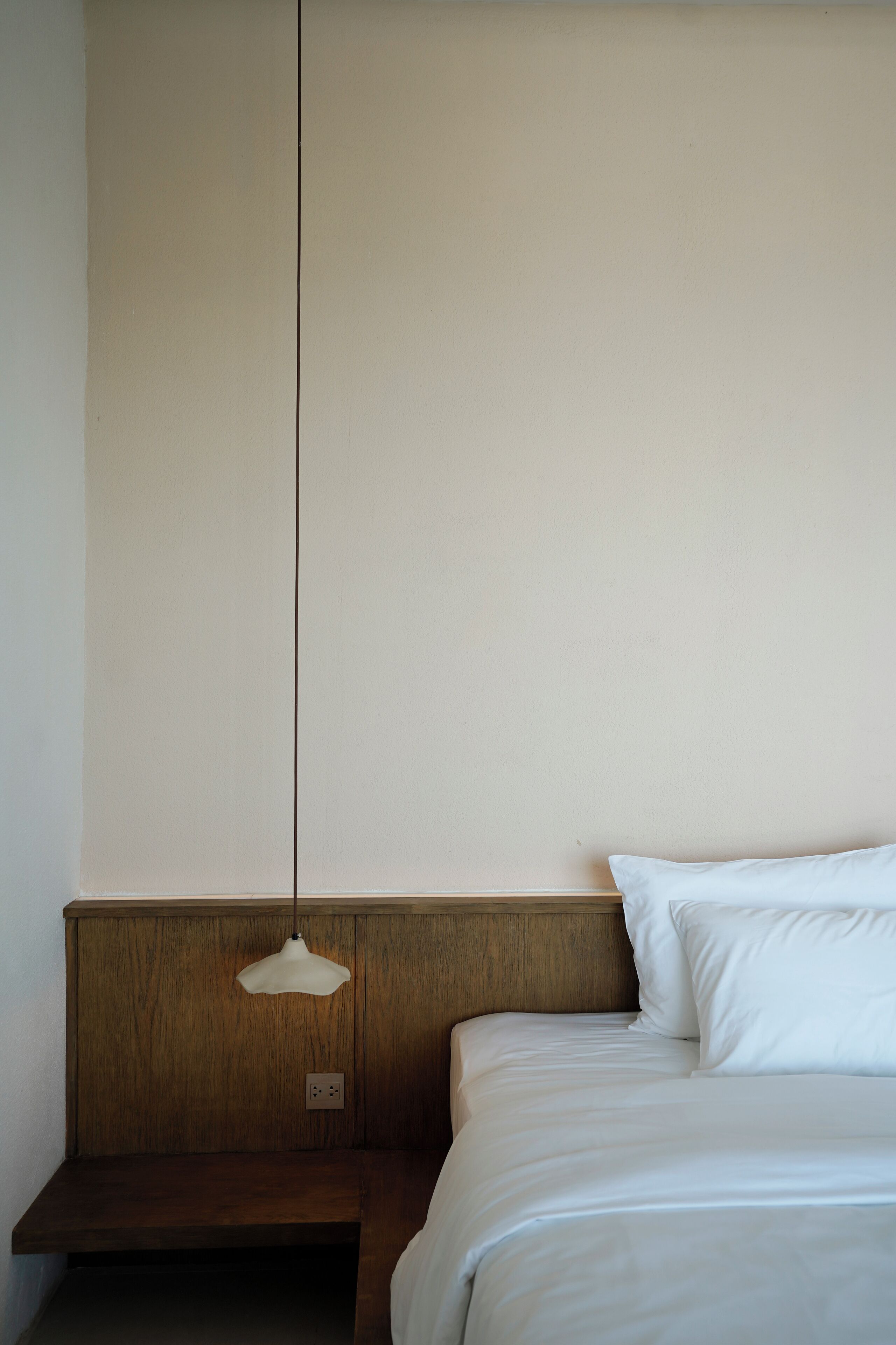 A bedroom with a wooden headboard, a bedside table, and a hanging light fixture.