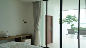 A hotel room with a bed, a bedside table with a kettle and cups, a wooden door, and a balcony with chairs. - Pichcha Kohlarn (Koh Lan)